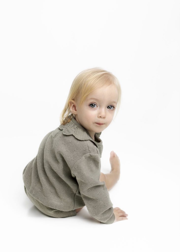 Little girl in green romper sitting backwards and looking over her shoulder by Flower Mound Photographer