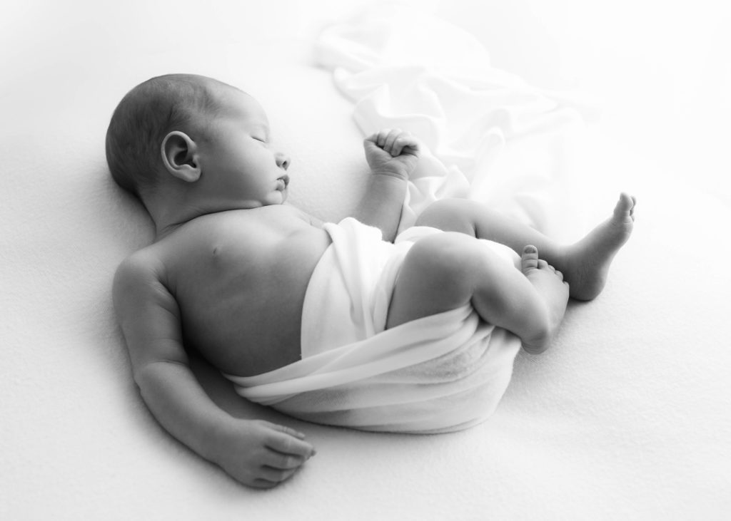 Newborn boy with white cloth loosely wrapped around him and trailing off in the background by Fort Worth Newborn Photographer