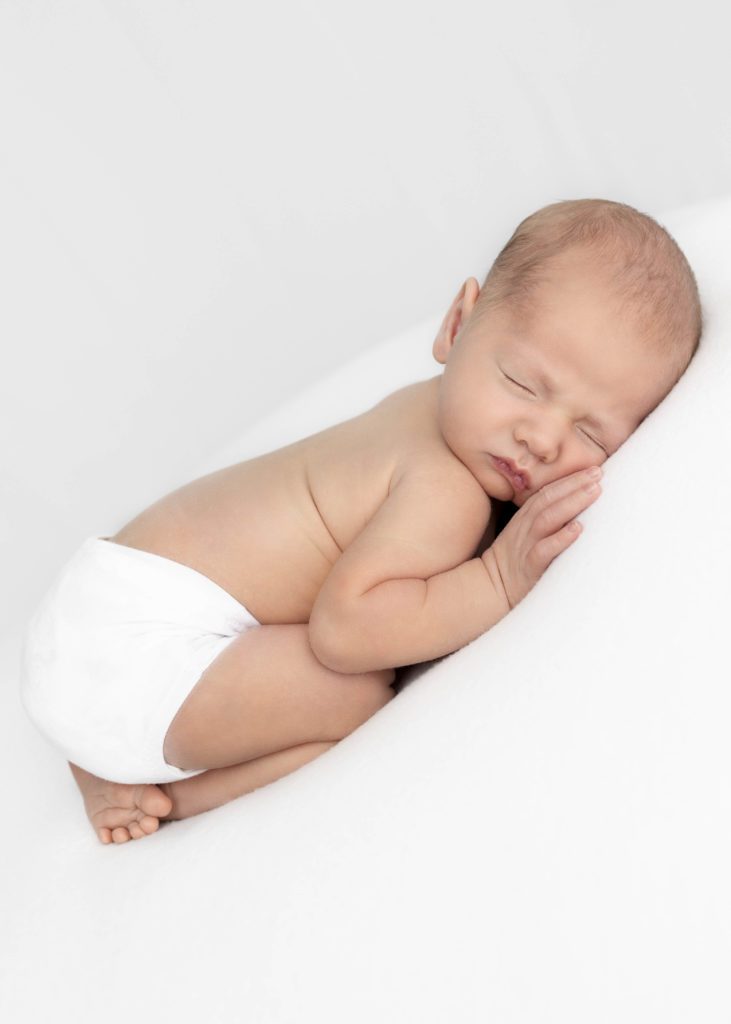 Newborn baby in just a white diaper cover sleeping on a white blanket