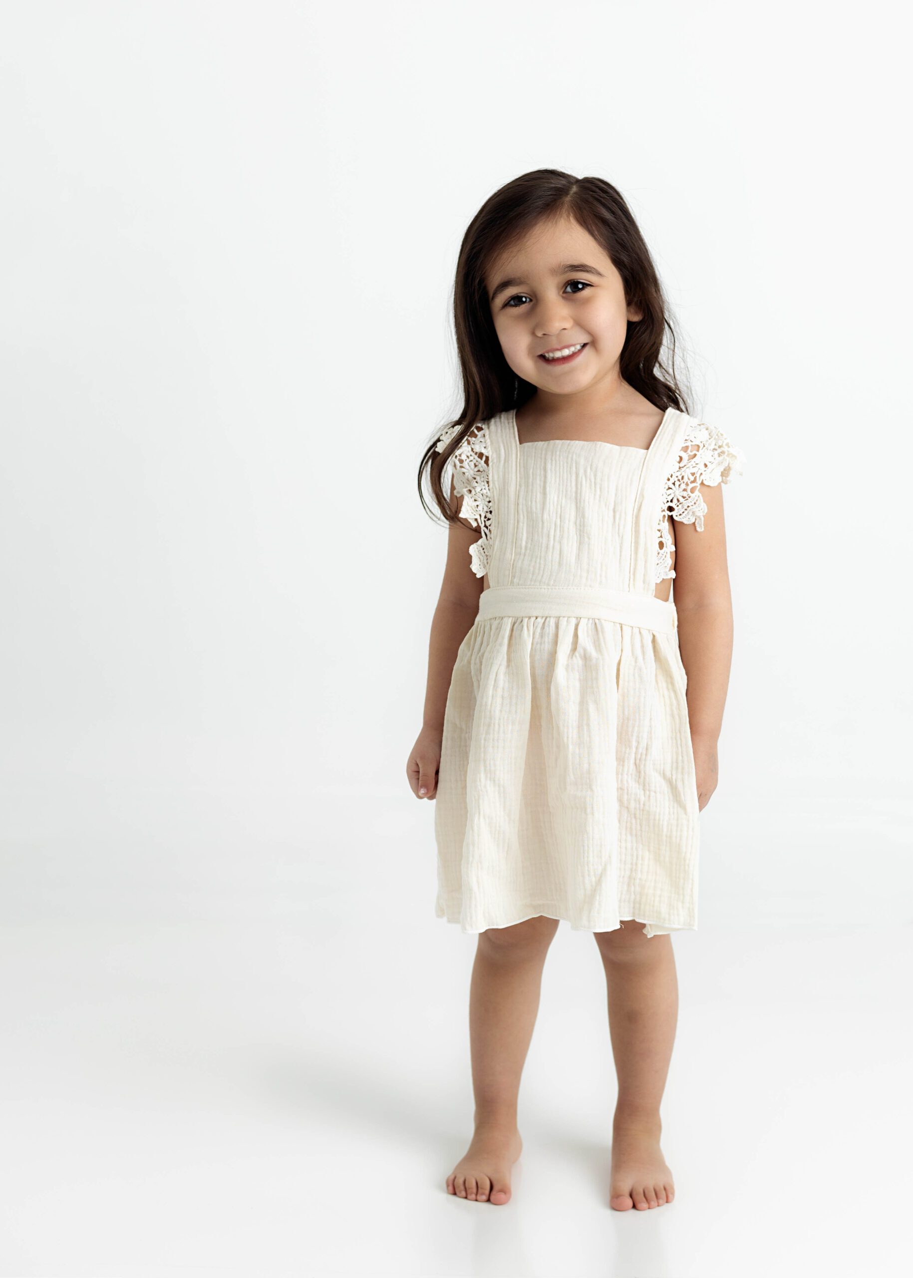 Little girl in white dress bashfully smiling for Dallas baby photographer