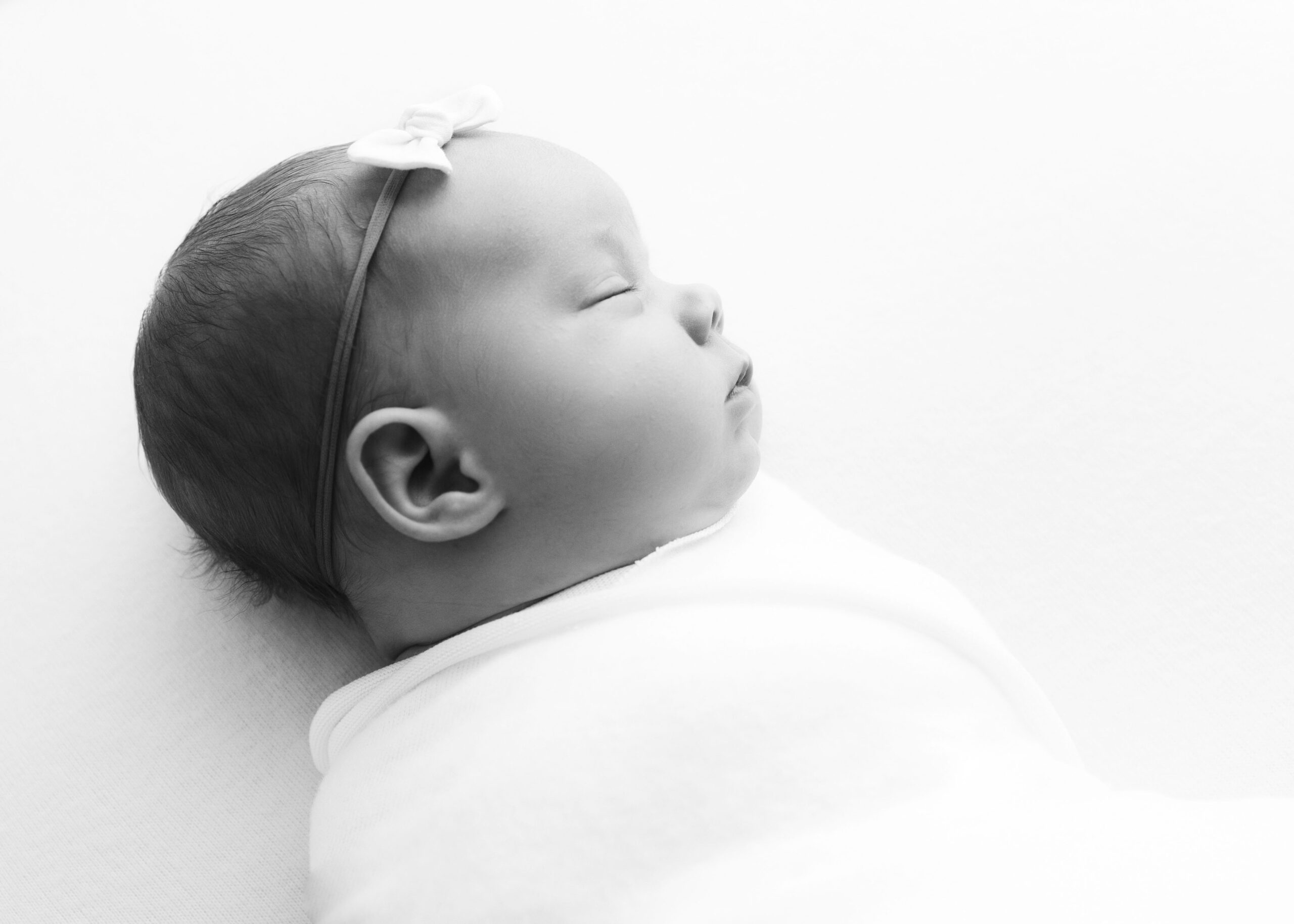 Sleeping newborn baby girl with white bow by baby photographer Dallas