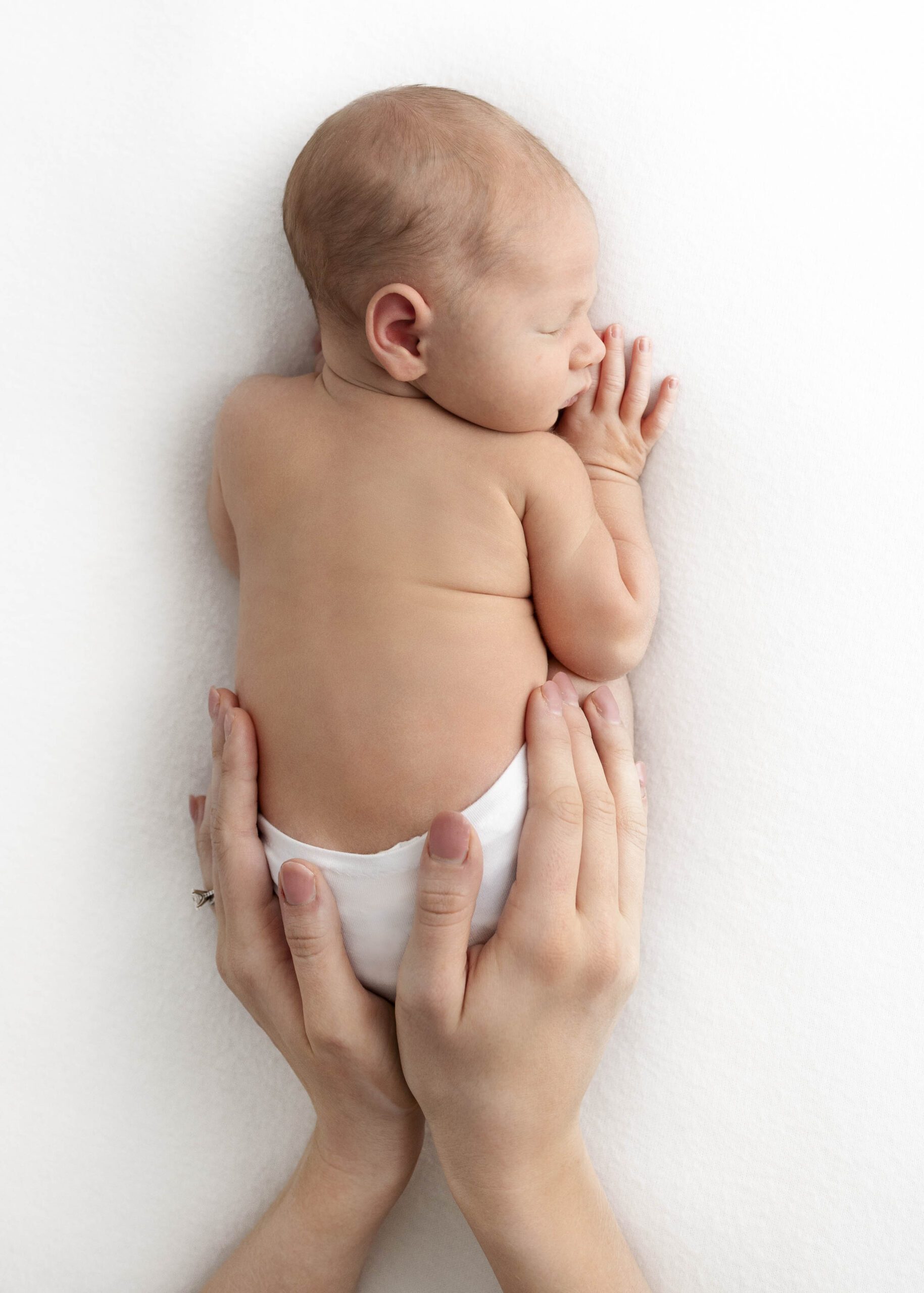 newborn baby with moms hands surrounding his bottom