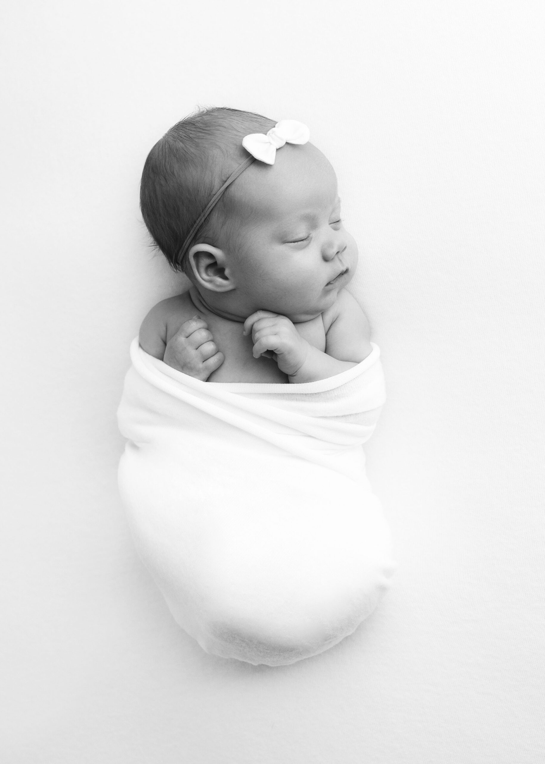 black and white photo of newborn wrapped in white blanket for best time newborn photos