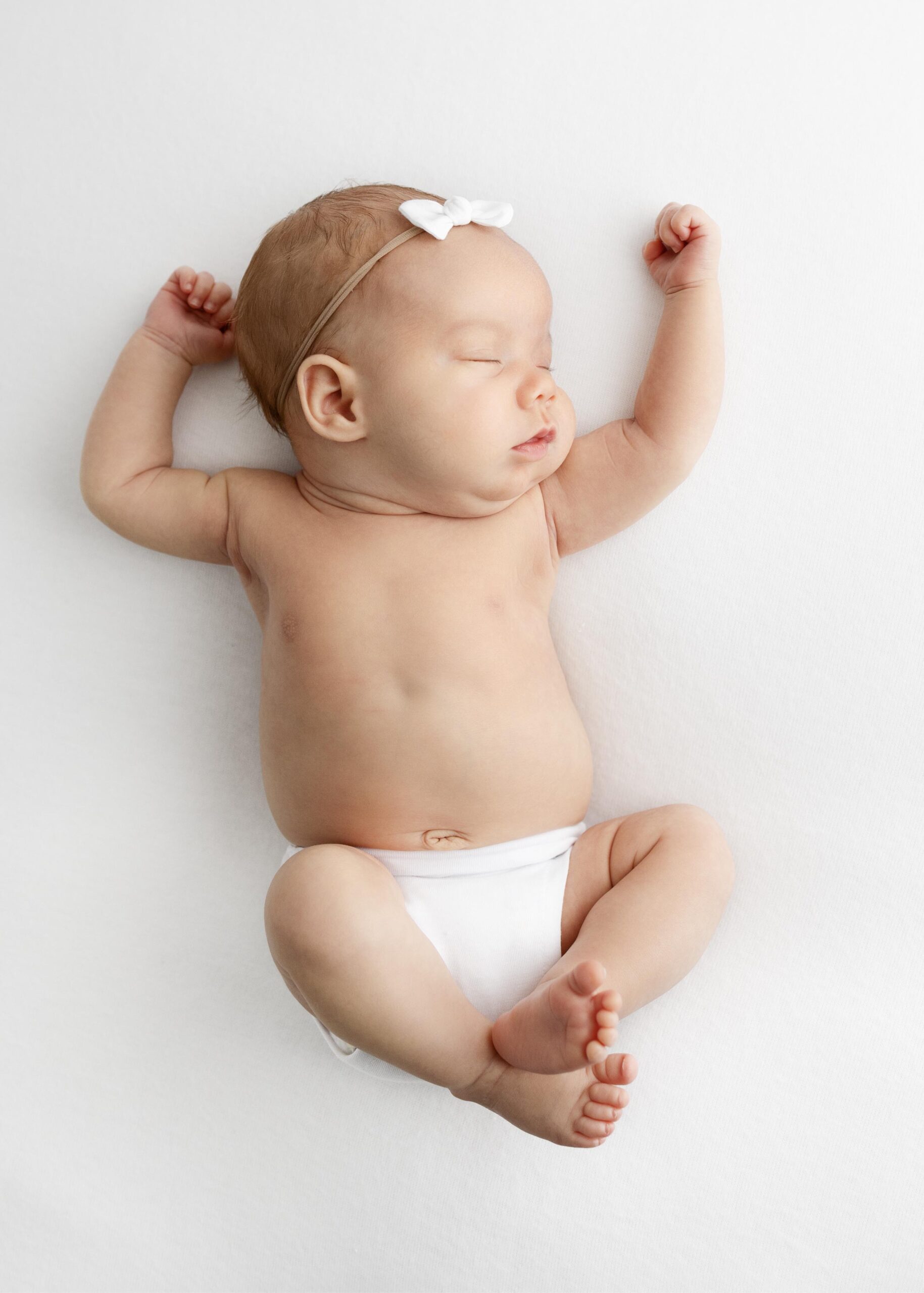 newborn girl in white diaper stretching while sleeping