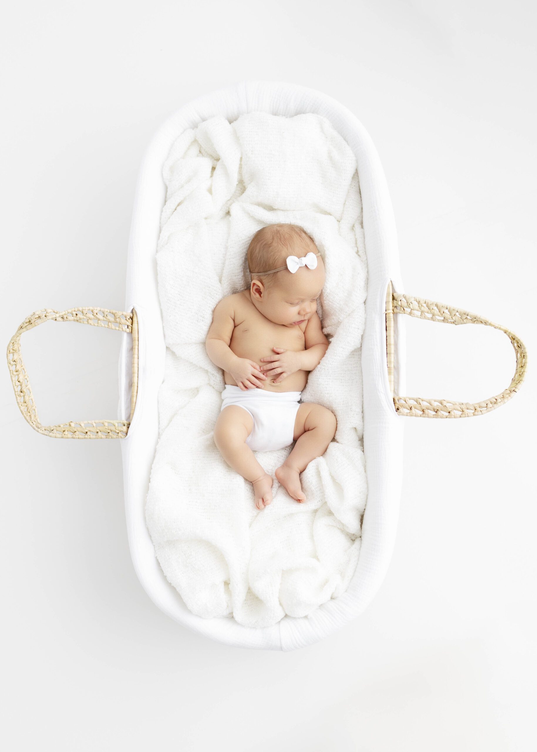 newborn baby in moses basket surrounded by white blankets for best time newborn photos