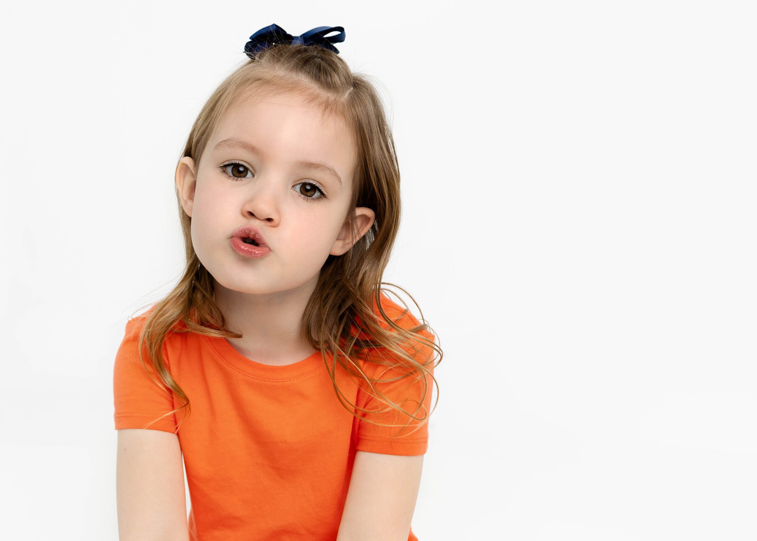 Little girl with orange dress on making a funny face by white studio photography