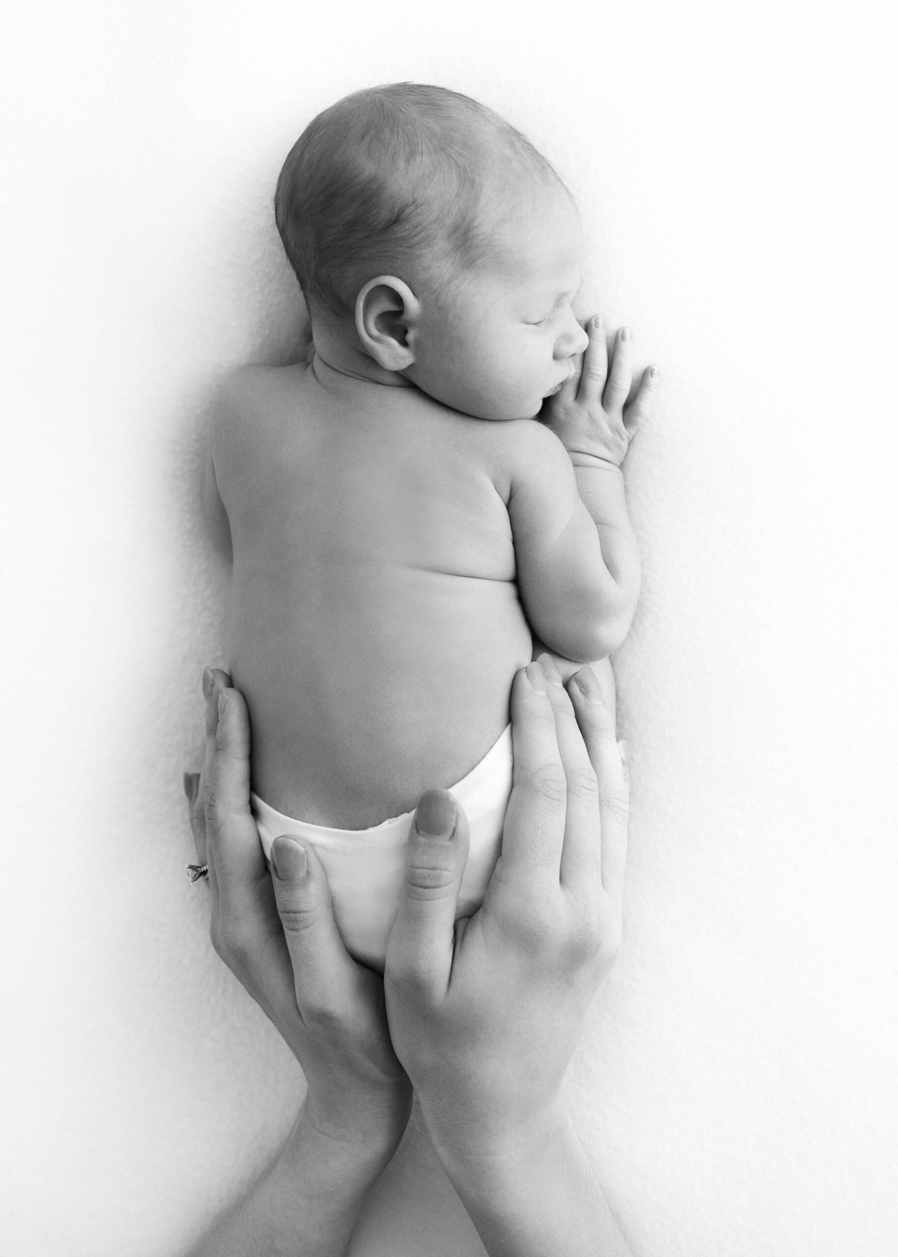 mom's hands around newborn's bottom as he sleeps on his belly by DFW newborn photographer