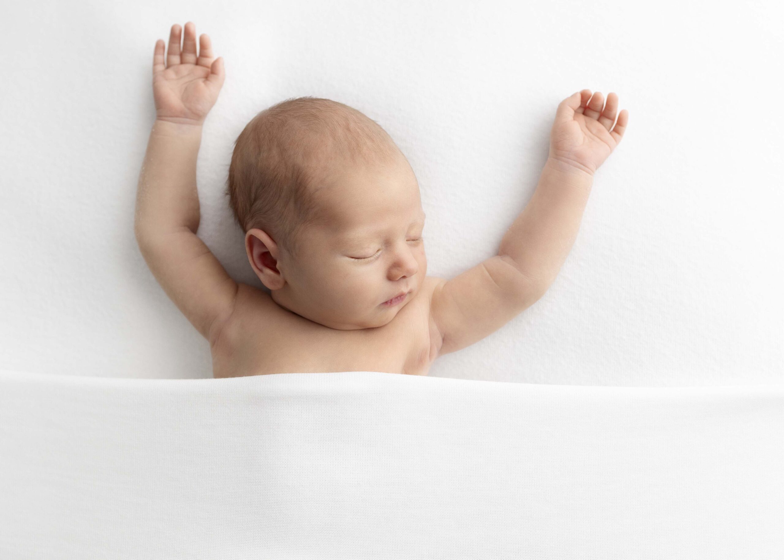 newborn baby under white blanket with arms outstretched