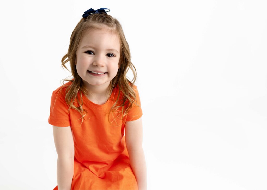 Little girl in orange dress smiling at the camera by Dallas portrait photography