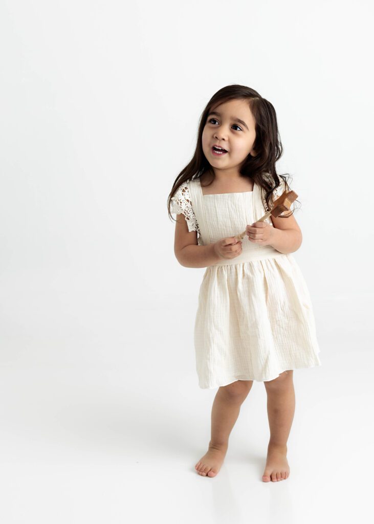 Toddler girl dancing for the camera in cream dress by Dallas portrait photography