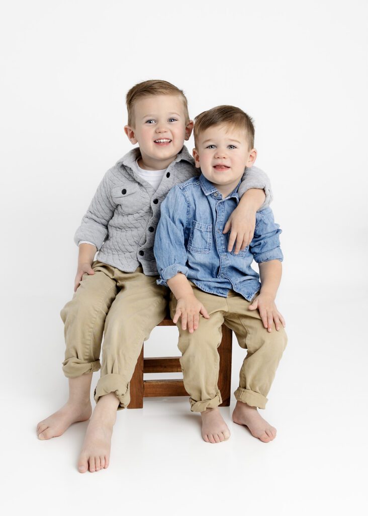 Toddler brothers sitting on a stool with arms around each other