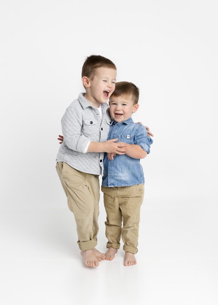 Toddler brothers holding on to one another and laughing by Dallas portrait photography