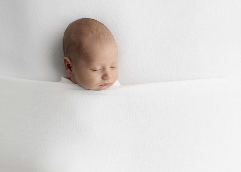 Sleeping newborn baby under a white blanket by newborn photography Dallas TX