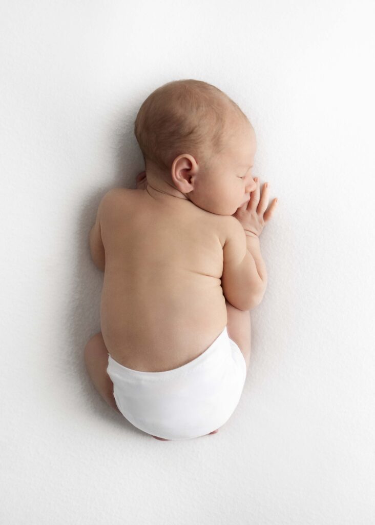 Newborn in white diaper sleeping on belly