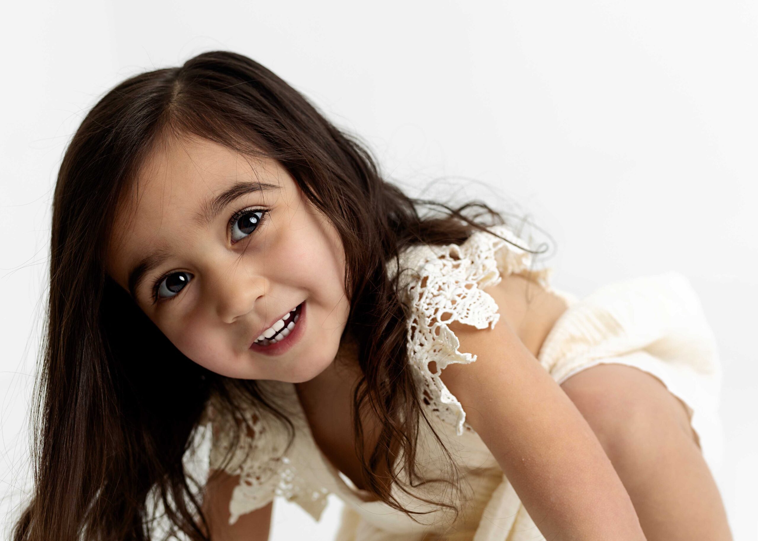 Little girl in cream dress about to stand up by photography studio Dallas TX