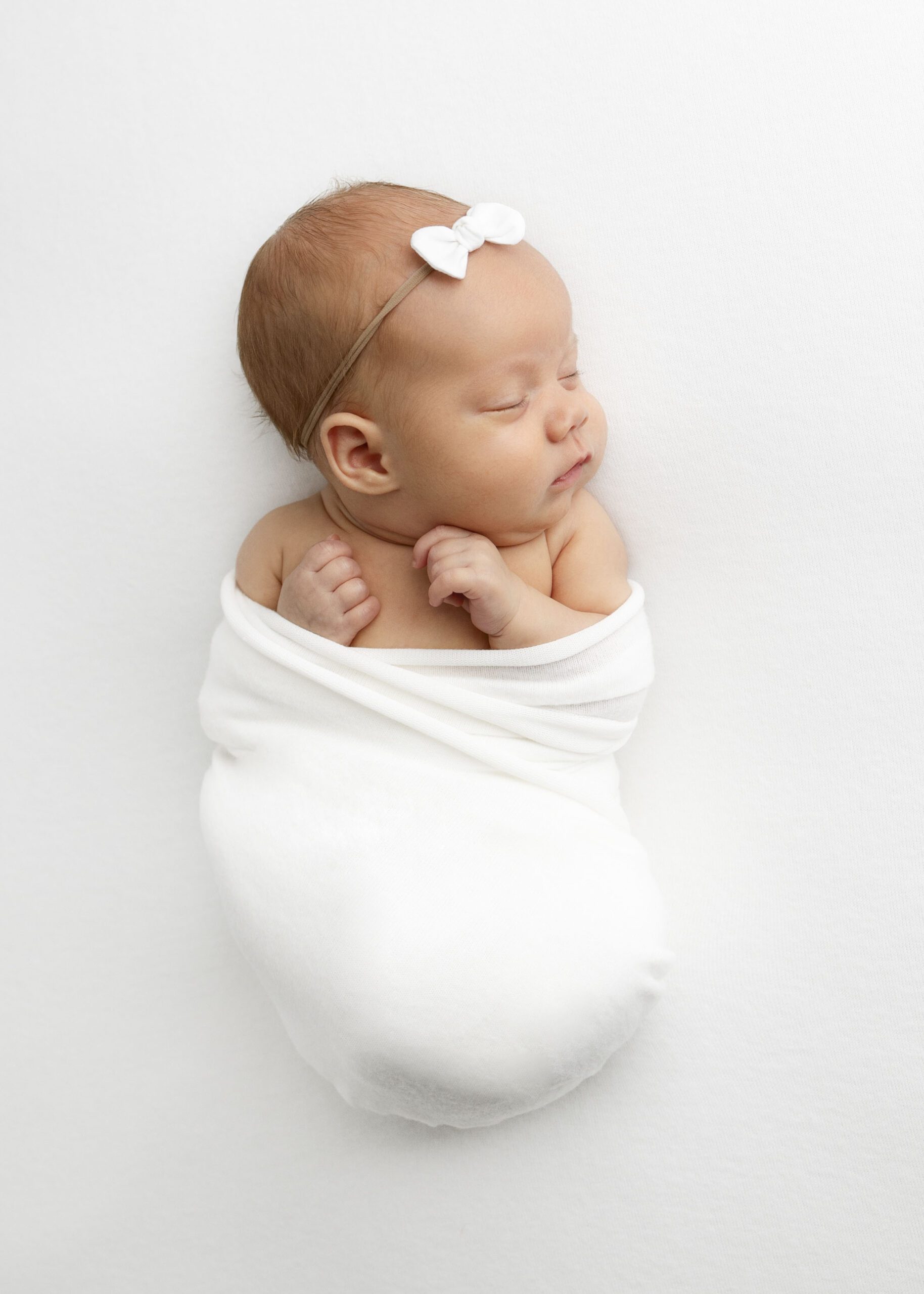 newborn girl wrapped in white blanket with white bow by Flower Mound Newborn photography