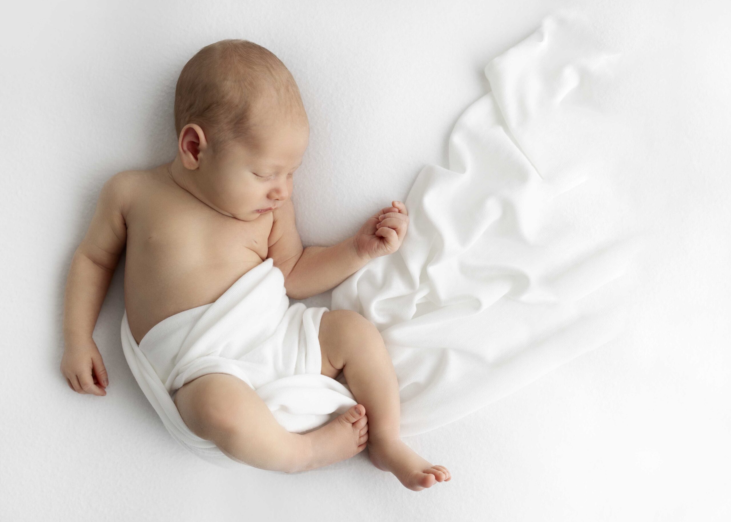 Newborn with white blanket trailing behind him while he sleeps