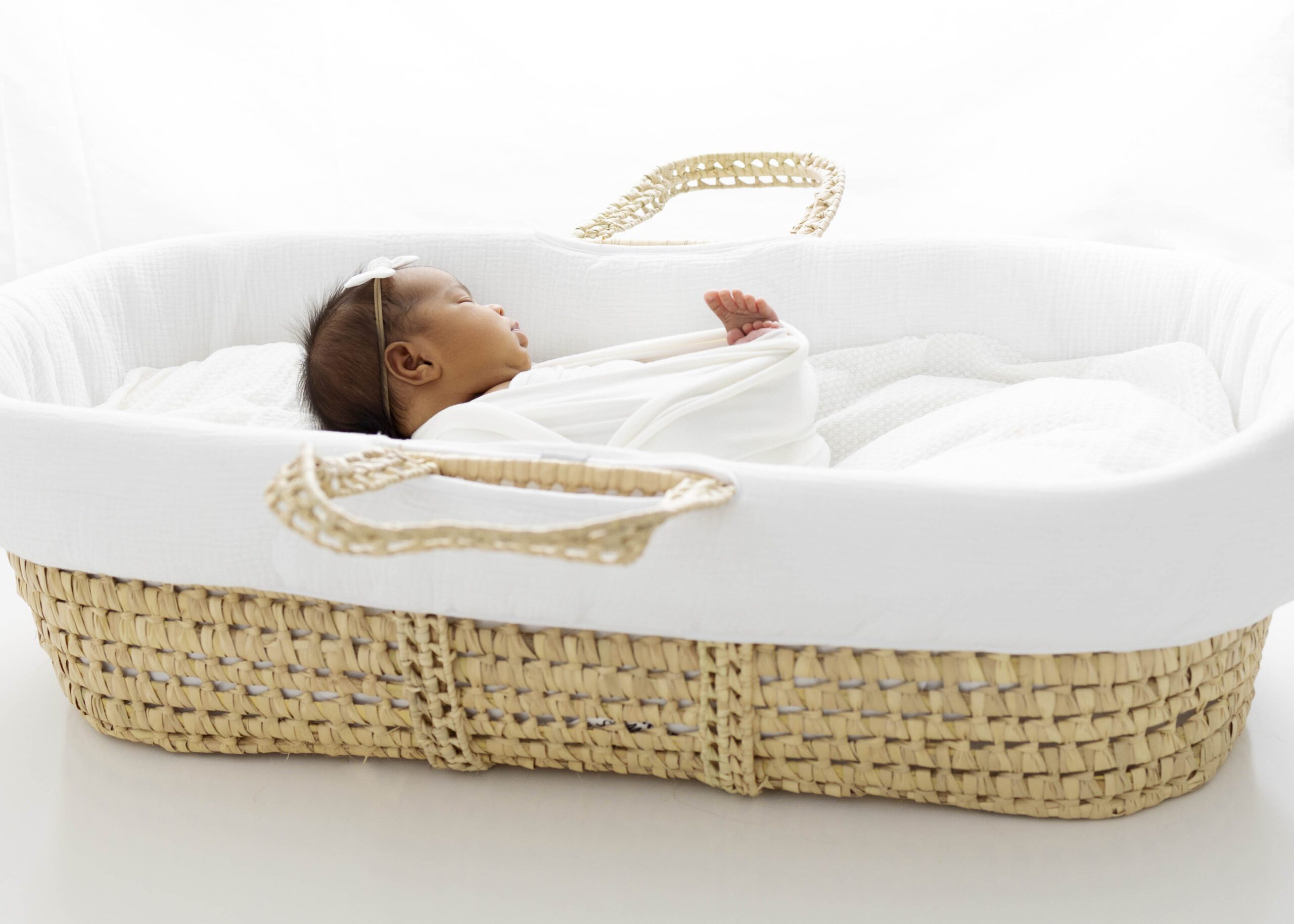newborn baby in moses basket with white blankets