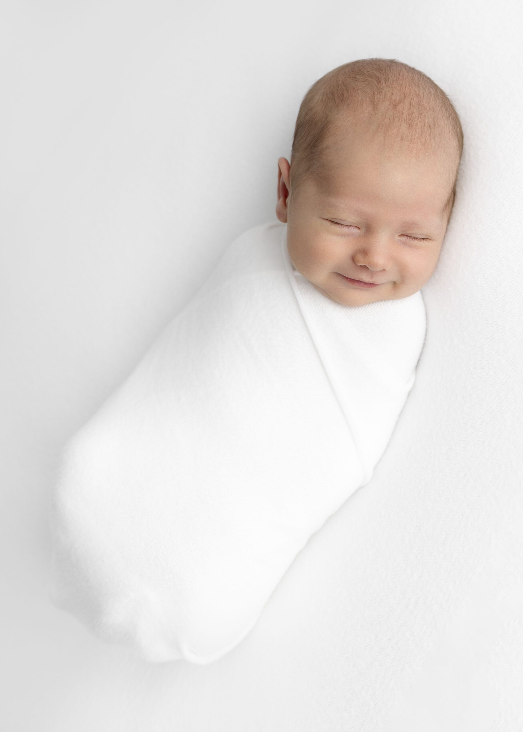 newborn baby swaddled and smiling at the camera