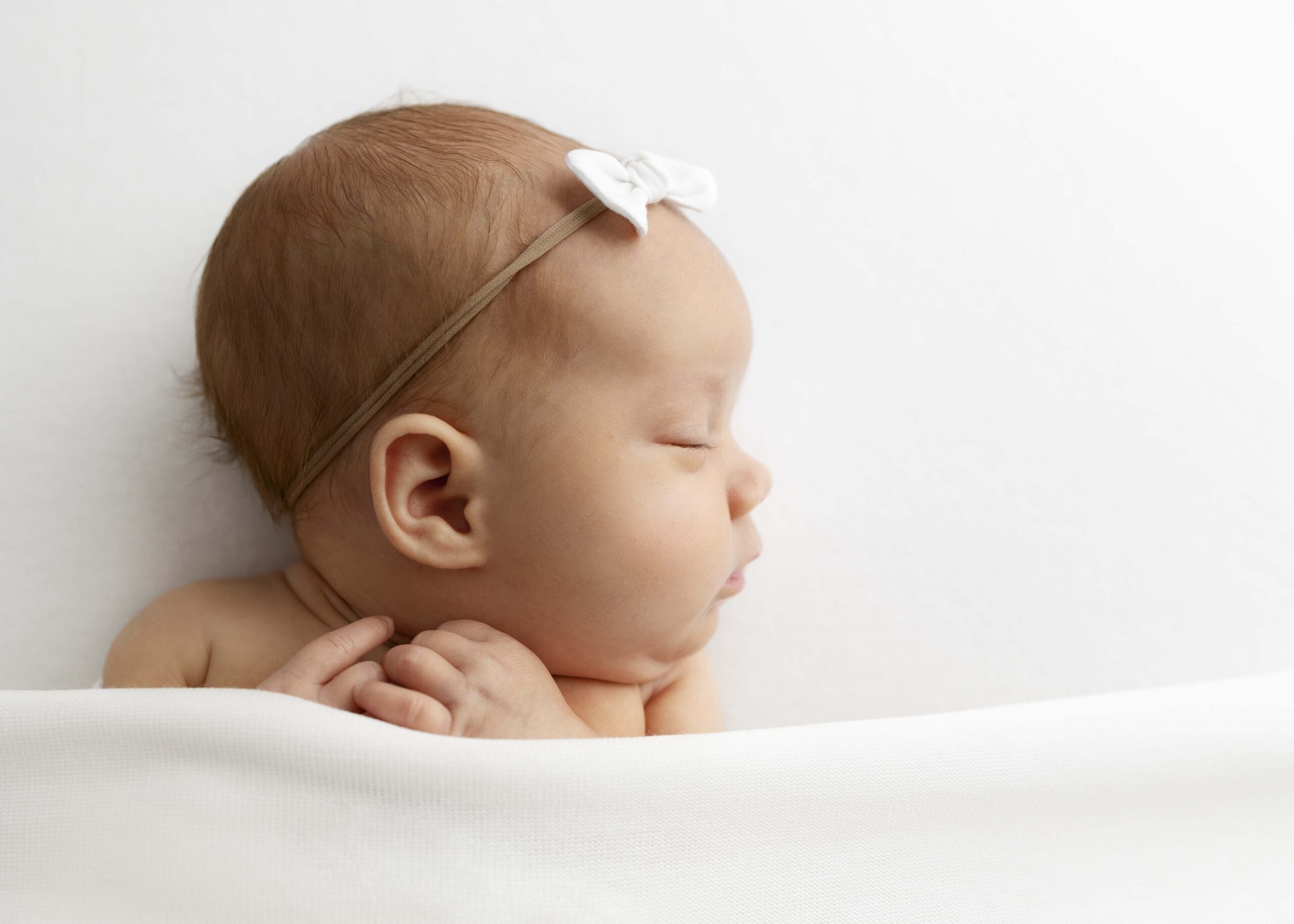 Newborn girl with white bow in hair sleeping