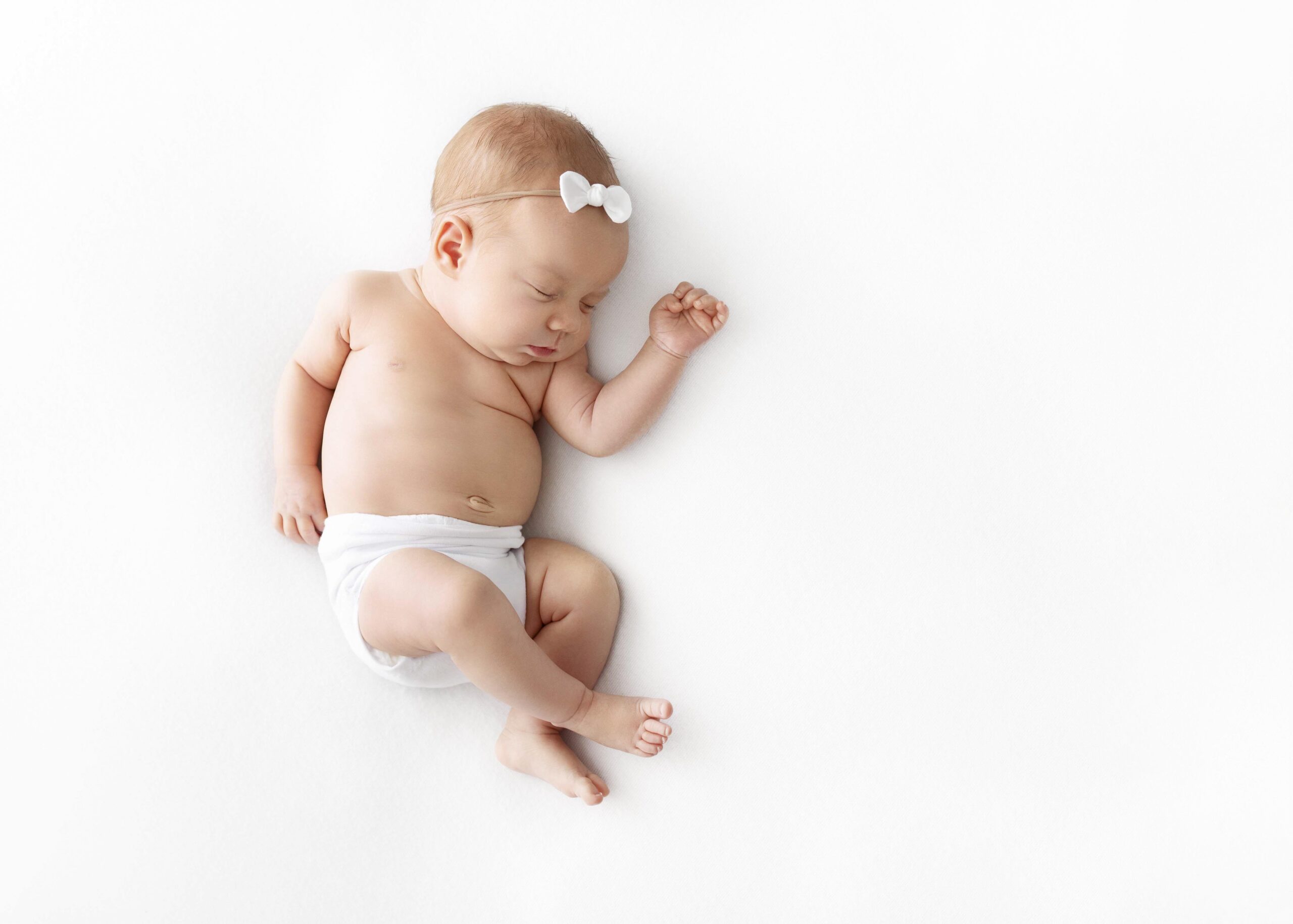newborn in white diaper sleeping on side by best newborn photographer