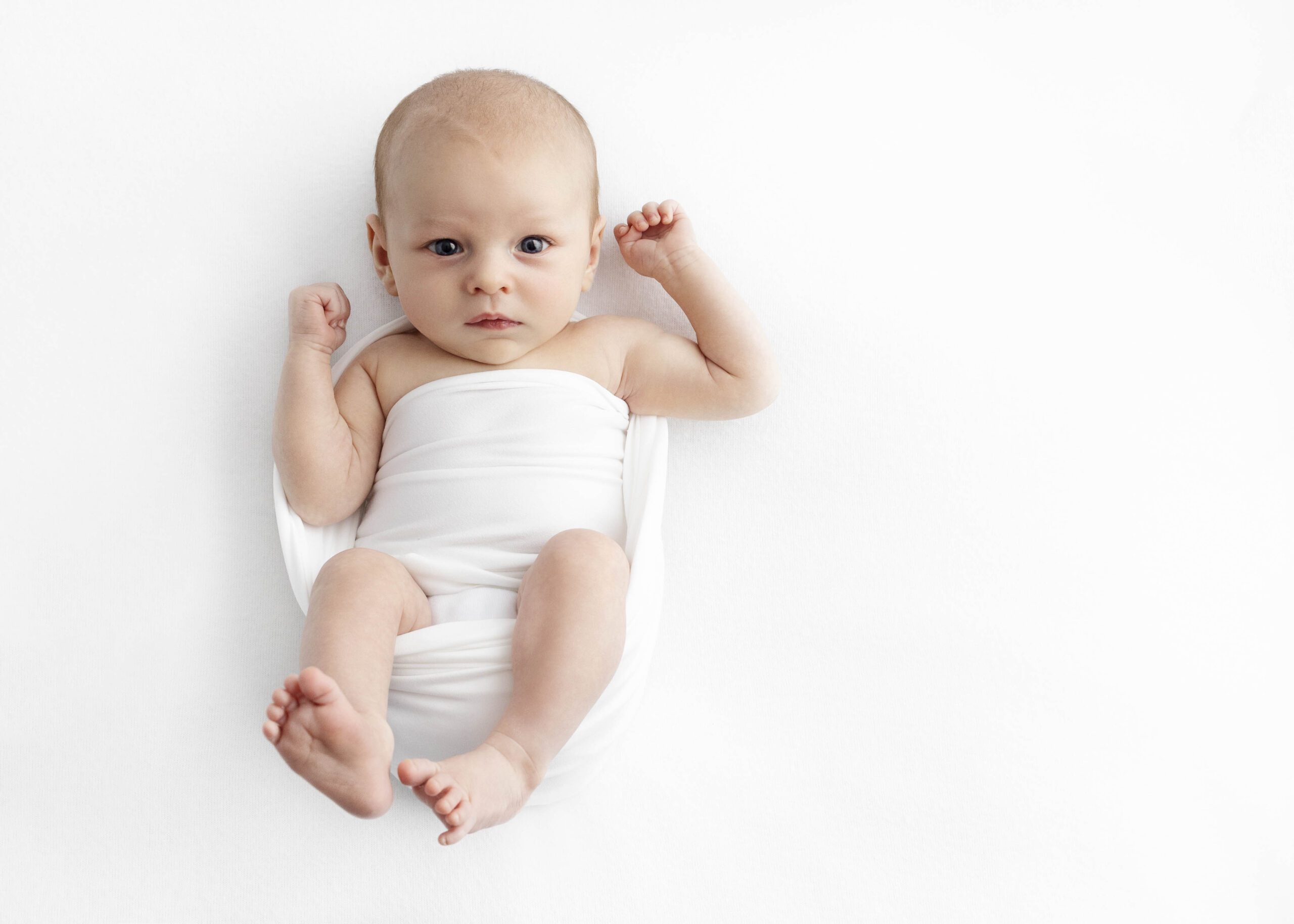newborn baby wrapped in white blanket by best newborn photographer in Dallas