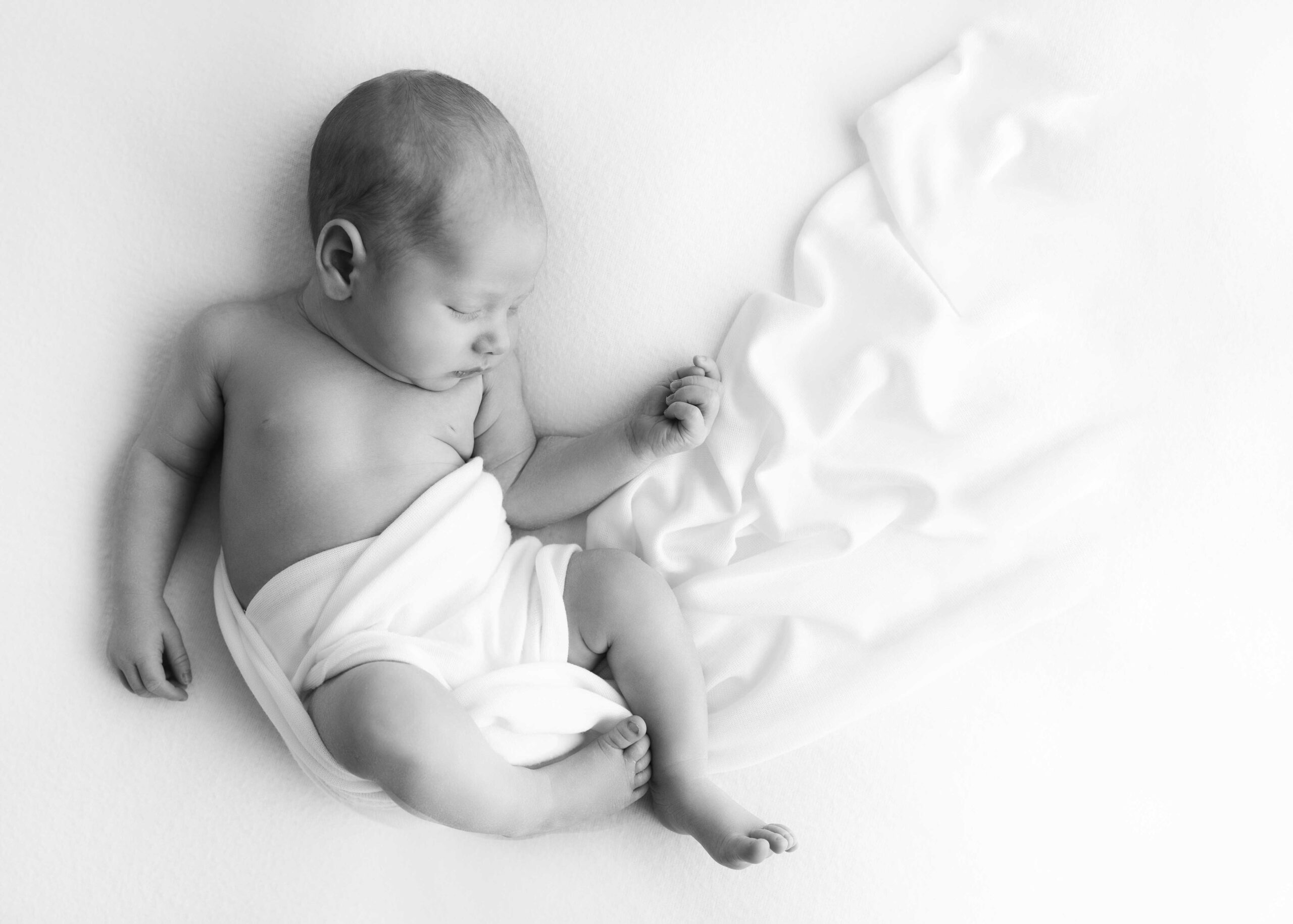 newborn baby with white blanket trailing around him as he sleeps by best newborn photographer in dallas