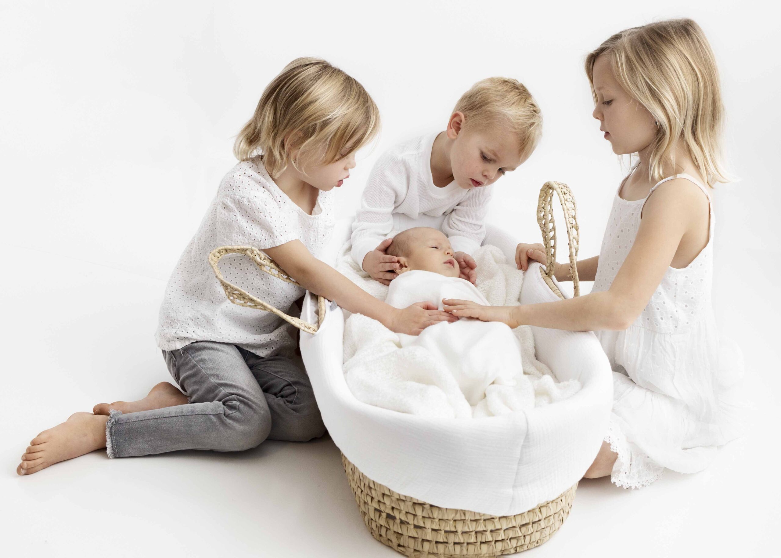 older siblings surrounding moses basket with newborn baby inside