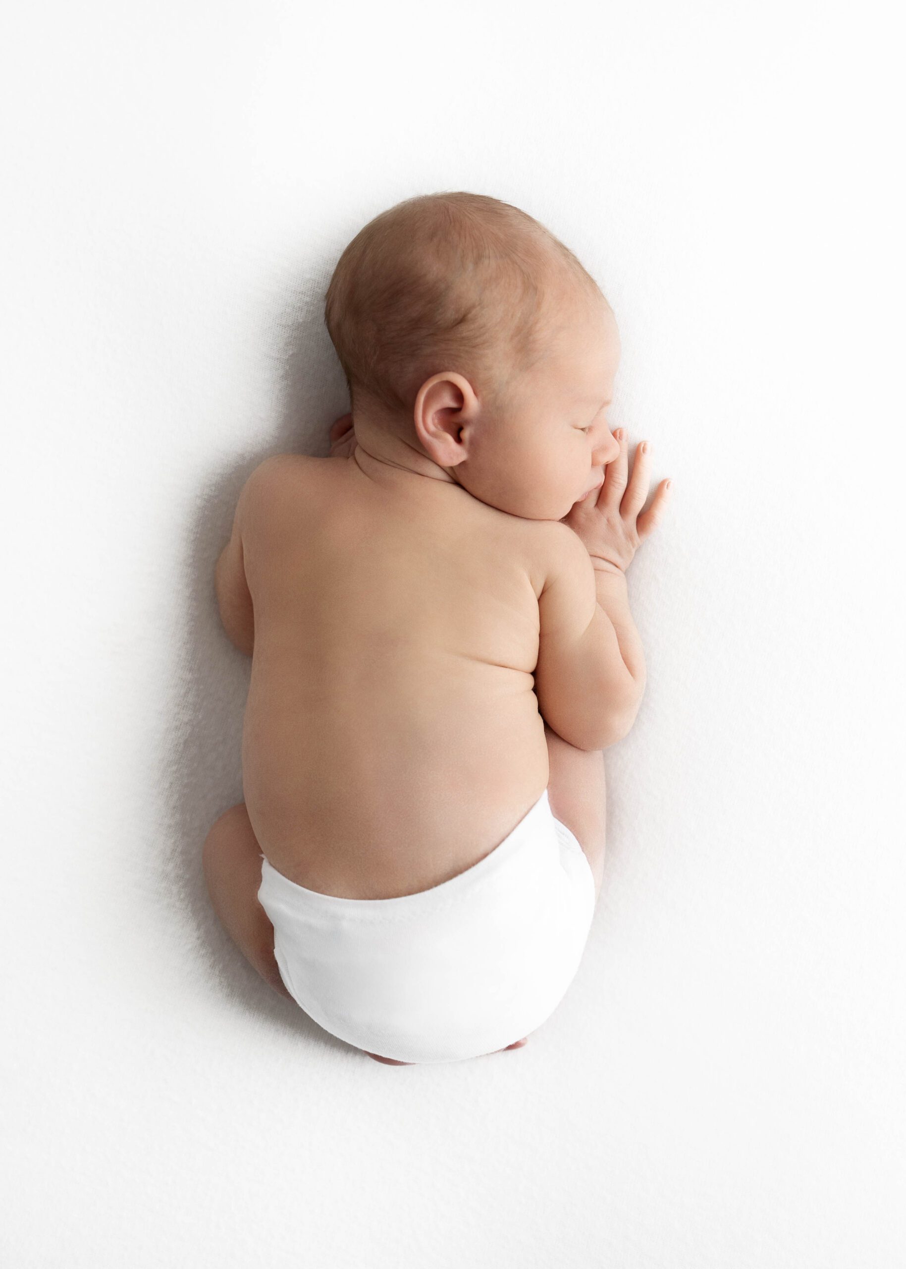 newborn with white diaper sleeping on tummy