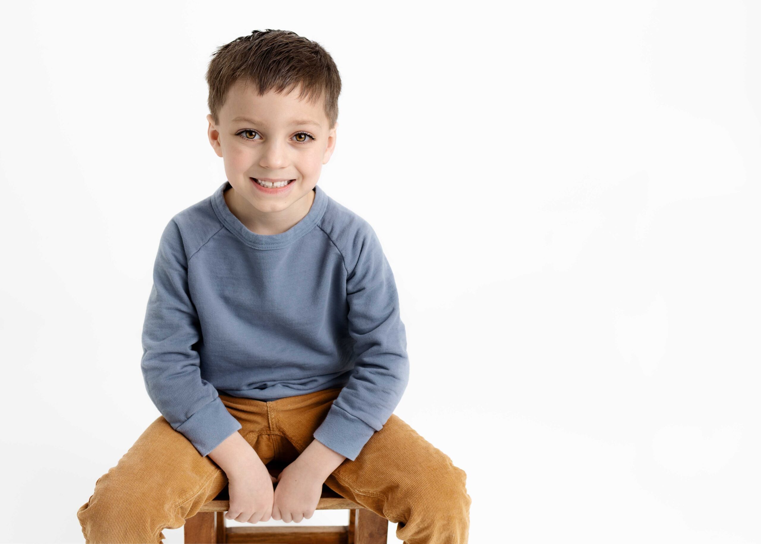 little boy sitting on stool smiling confidently at the camera
