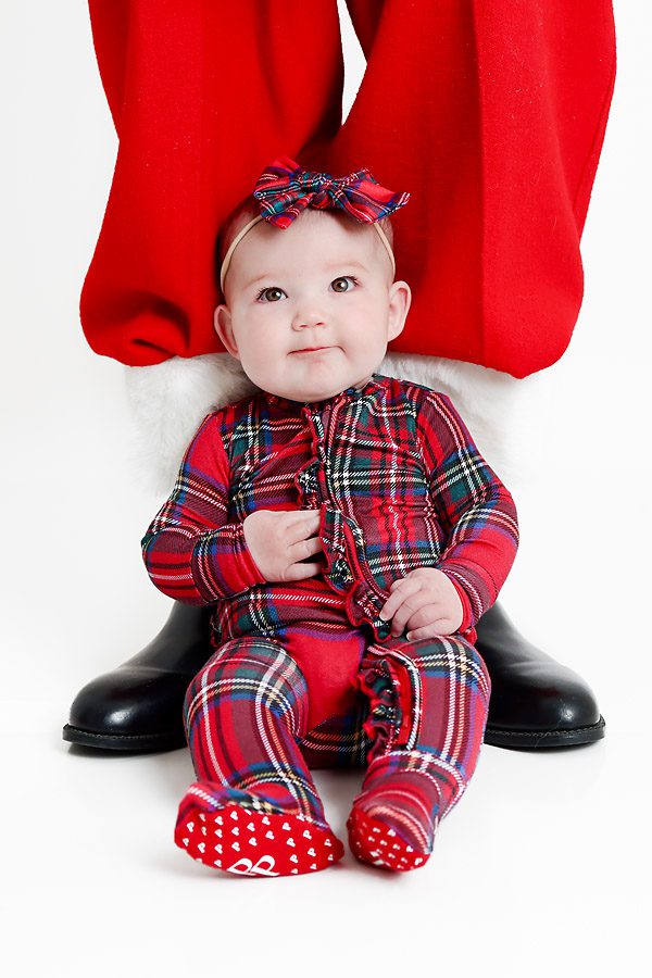 Baby girl in Christmas pajamas sitting on Santa's boots for pictures with Santa Dallas, TX