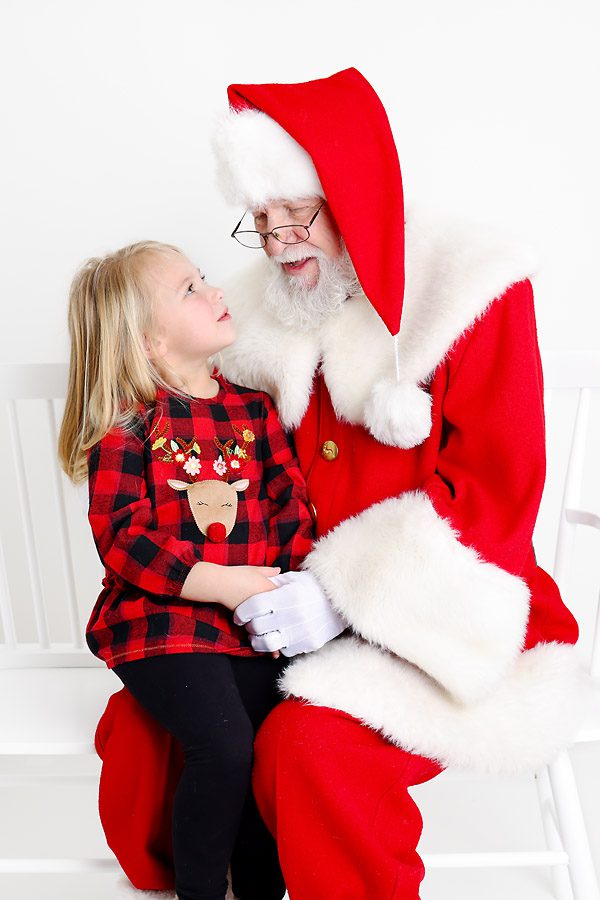 Little girl sitting on Santa's lap talking to him