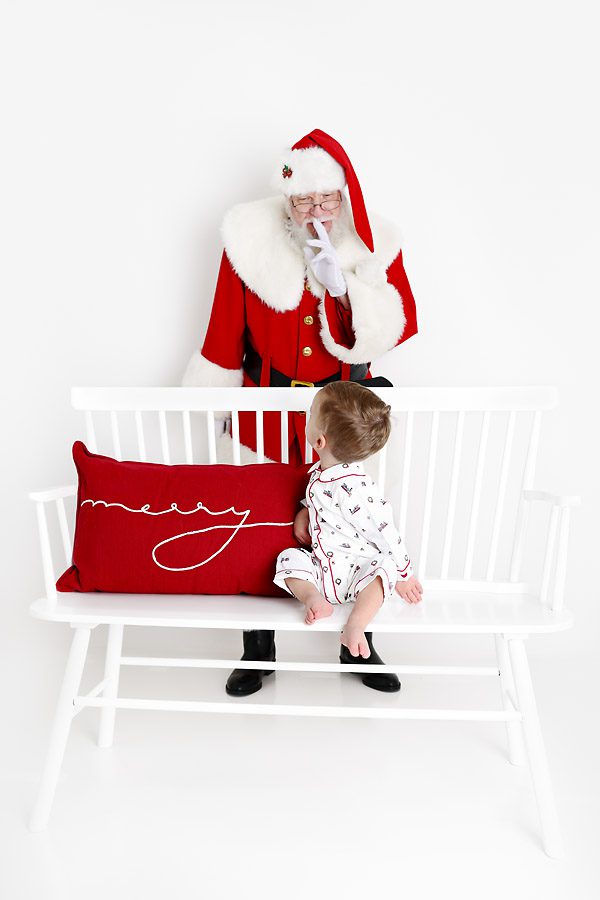 Santa behind a little boy who is sitting on a bench