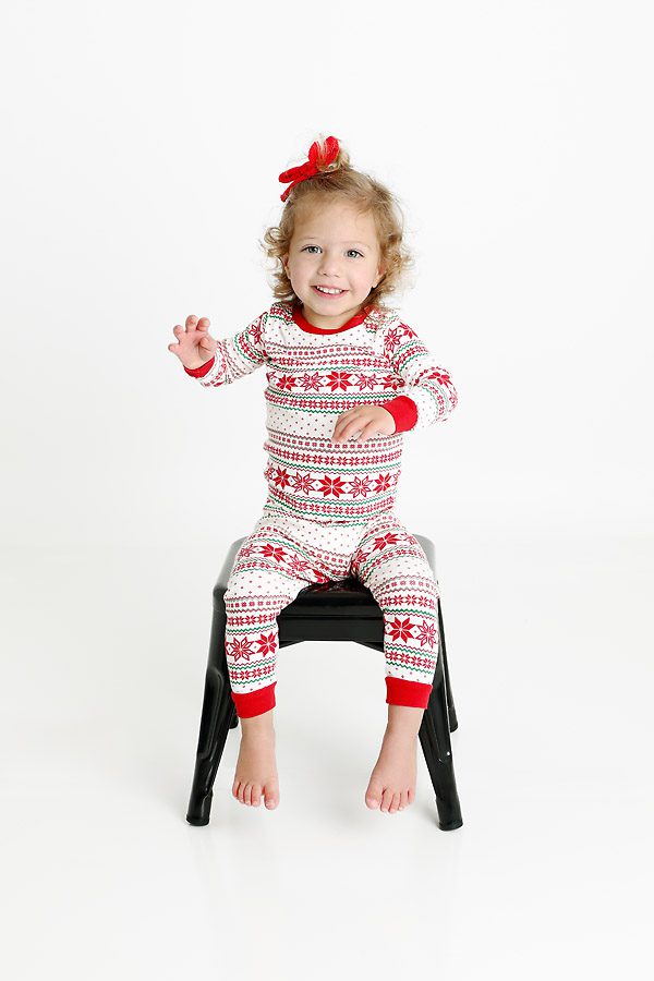 Little girl on a black stool in Christmas pajamas